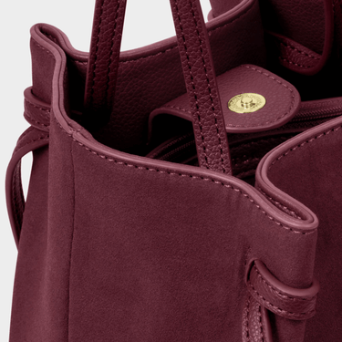 Close-up of a burgundy handbag with a gold clasp on a light gray background