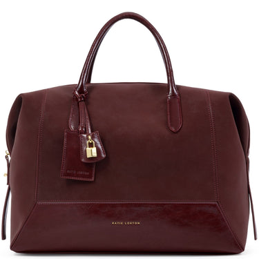 A dark burgundy leather handbag by Katie Loxton, featuring dual top handles, a hanging leather tag with a gold padlock, and gold brand lettering on the lower front, set against a plain white background.