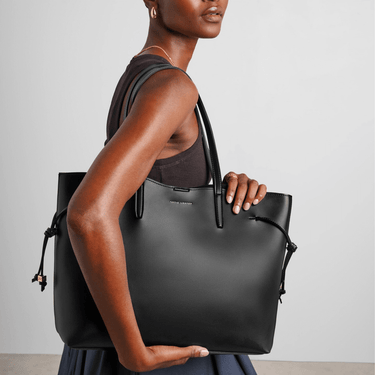 Woman holding a black handbag against a plain background