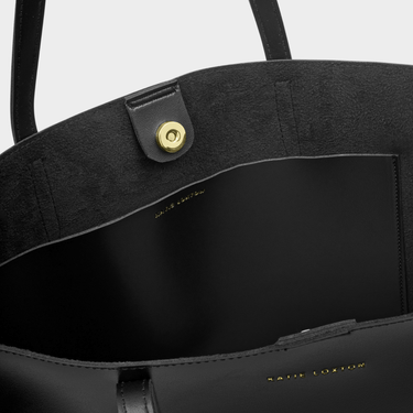 Close-up of a black leather handbag with gold hardware on a light gray background