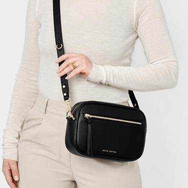 Person holding a black crossbody bag with gold accents on a white background