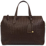 A dark brown woven leather handbag with double top handles, a hanging leather tag, and gold-tone hardware, photographed on a clean white background.