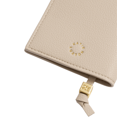 Close-up of a beige leather passport cover with a gold logo and strap on a white background