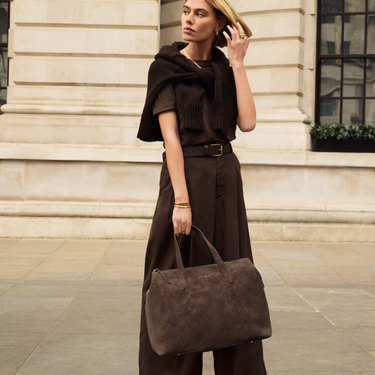 Woman in a brown outfit holding a matching bag outdoors.