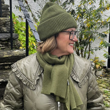 Person wearing a green beanie and scarf standing outdoors with stone steps and building in the background