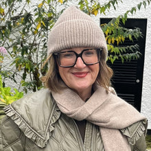 Person wearing a green puffer jacket, beige hat, and scarf standing outdoors.
