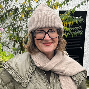 Person wearing a green puffer jacket, beige hat, and scarf standing outdoors.