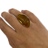 Hand wearing a gold ring with a large brown stone on a white background
