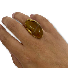 Hand wearing a gold ring with a large brown stone on a white background