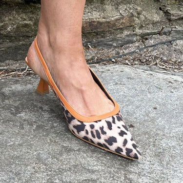 Leopard print shoes with orange accents worn by a person on a stone surface.