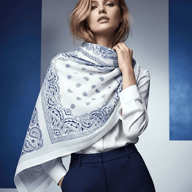 Woman wearing a white shirt and blue pants with a white scarf featuring blue patterns.