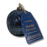 A dark blue textured glass candle jar with a hanging blue tag that reads 'Osmology Nordic Fireside.' on a white background.