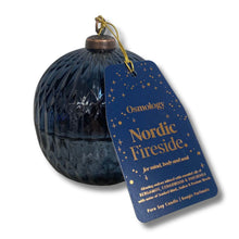 A dark blue textured glass candle jar with a hanging blue tag that reads 'Osmology Nordic Fireside.' on a white background.
