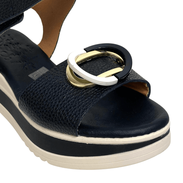 Black sandal with gold and white buckle on a white background