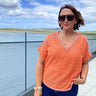 Woman wearing an orange patterned shirt and sunglasses outdoors with a scenic background