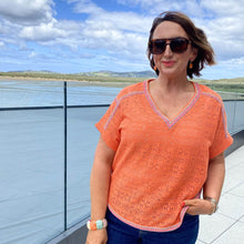 Woman wearing an orange patterned shirt and sunglasses outdoors with a scenic background