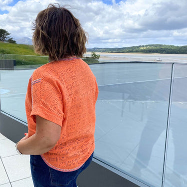 Person wearing an orange shirt looking out over a scenic landscape from a balcony.