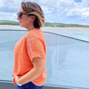 Woman in an orange top standing on a boat with a scenic background