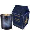 A lit Osmology Nordic Fireside candle in a dark blue speckled glass holder, shown next to its matching house-shaped packaging box with gold star and text details on a white background.