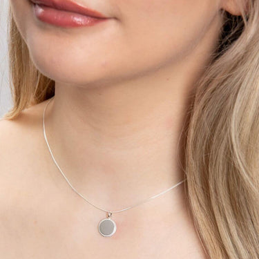 Close-up of a person wearing a silver necklace with a round pendant.
