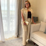 Woman in beige sleeveless top and pants standing in a living room.