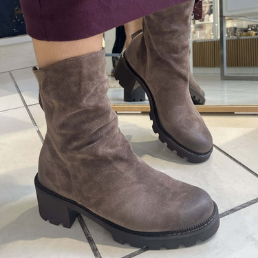 A person wearing a dark purple skirt and brown suede ankle boots with chunky black soles, standing on a tiled floor in a store.