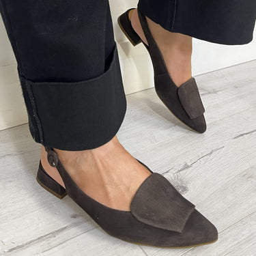 Person wearing black pants and brown pointed-toe flats on a light wooden floor.