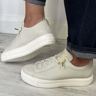 off white sneakers worn with dark jeans on a light wooden floor.
