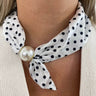 White polka dot scarf with a large pearl knot worn around the neck.