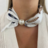 Necklace with a pearl and a patterned scarf around the neck against a neutral background