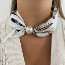 Necklace with a pearl and a patterned scarf around the neck against a neutral background