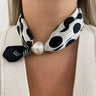 Black and white polka dot scarf with a pearl accent around a person's neck.