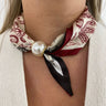 Necklace with a patterned scarf and pearl-like bead worn by a person.