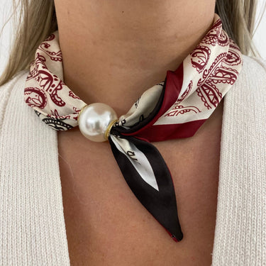 Necklace with a patterned scarf and pearl-like bead worn by a person.