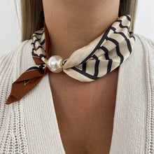 Necklace with a beige and black patterned scarf and pearl-like bead on a person wearing a white sweater.