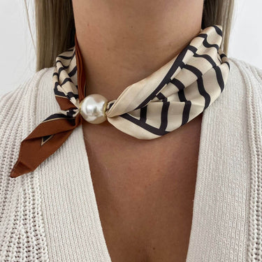 Necklace with a beige and black patterned scarf and pearl-like bead on a person wearing a white sweater.