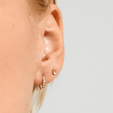 Close-up of an ear wearing two earrings against a light background