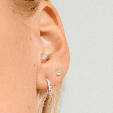 Close-up of an ear wearing a diamond stud earring on a plain background
