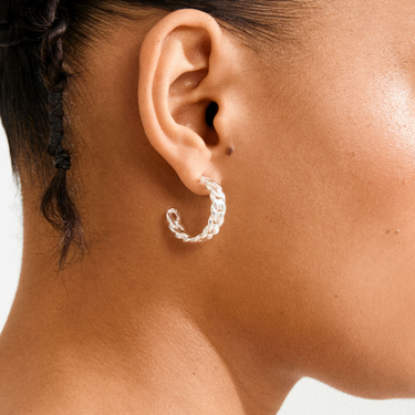 Close-up of an ear wearing a silver hoop earring with a blurred background