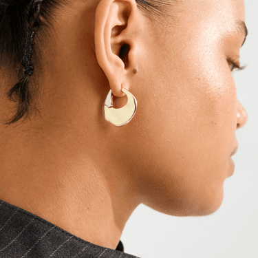 Close-up of a person wearing a gold hoop earring on a neutral background