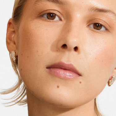 Close-up of a person wearing gold earrings with a plain background