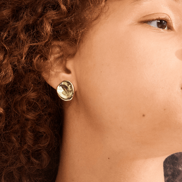 Close-up of a person wearing a gold earring with a green gemstone.