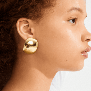 Close-up of a person wearing a gold earring on a white background