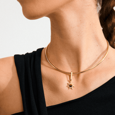 Gold necklace with a sun pendant worn by a person against a neutral background