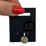 A silver-toned circular charm with an engraved double-heart design, attached to a black Pilgrim brand display card. A hand with red nail polish is holding the top of the card against a plain white background.