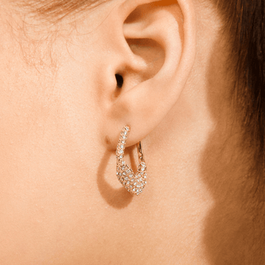 Close-up of an ear wearing a sparkling hoop earring on a neutral background