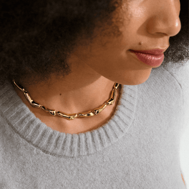 Close-up of a person wearing a gold chain necklace with a gray sweater.