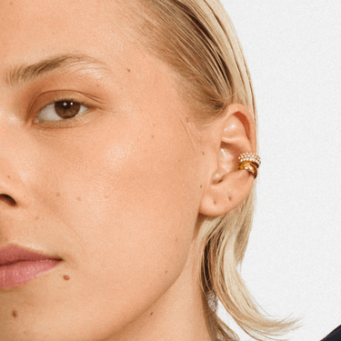 Close-up of a person wearing a gold earring on a white background