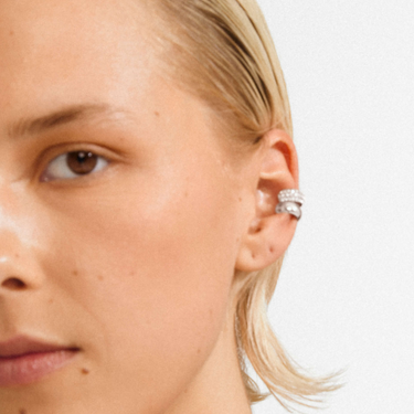 Close-up of a person wearing a silver earring on a plain background