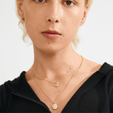 Close-up of a person wearing two gold necklaces on a plain background